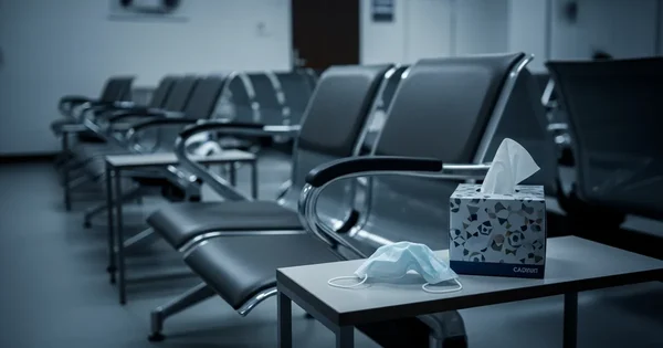 A mask and tissues sit on a table in an empty waiting room.