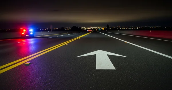 Police car sits on a highway at night with lights flashing.
