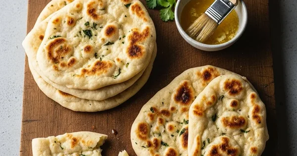 Freshly baked naan bread sits on a wooden cutting board with melted butter.
