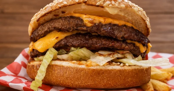 A double cheeseburger with lettuce sits on a checkered paper with french fries.