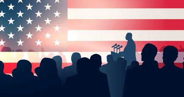 A speaker addresses a crowd with the American flag in the background.