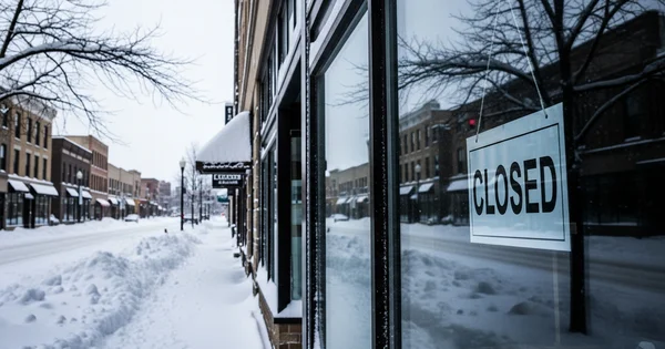 A closed sign hangs in a store window on a snow-covered street.