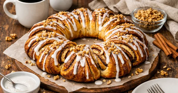 A cinnamon roll wreath sits on a table next to coffee and cinnamon sticks.