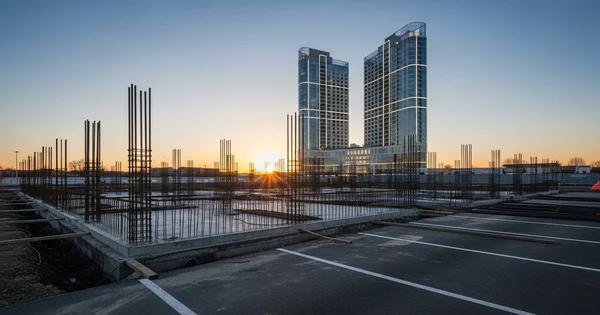 Construction continues on a new high-rise development as the sun sets over existing skyscrapers.