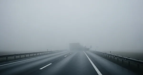 A truck drives on a highway in heavy fog.