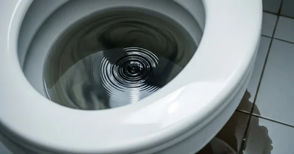 Water swirls in a toilet bowl. Water has leaked onto the surrounding floor.