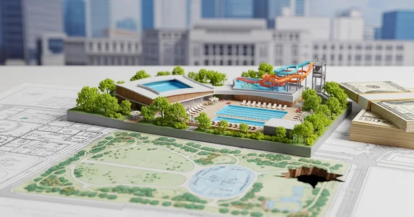 Architectural model of a park and pool area sits on top of a blueprint with stacks of money nearby.