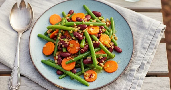 A plate of green bean salad with kidney beans and carrots is ready to be served.