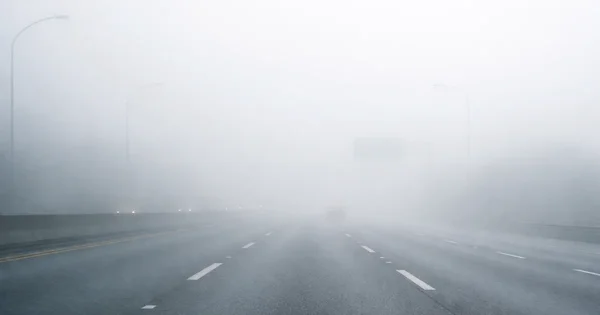 A vehicle travels on a highway with limited visibility due to heavy fog.