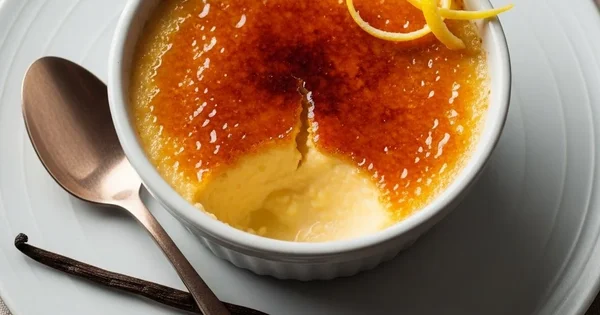 A creme brulee dessert is served with a vanilla bean and spoon.