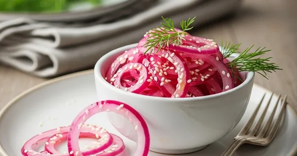 A bowl of pickled red onions with sesame seeds and dill sits on a plate with a fork.