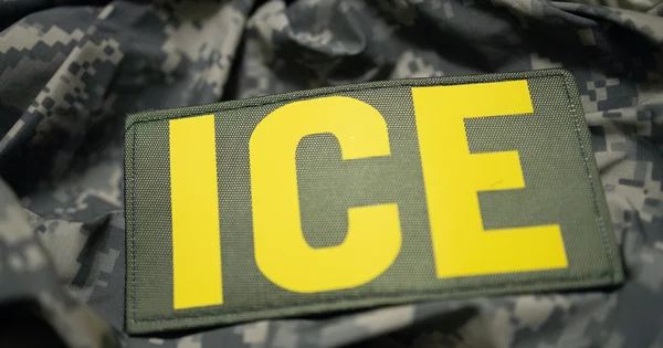 A patch with the letters ICE is displayed on a camouflage uniform.