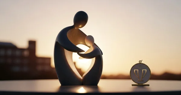 A sculpture of an embrace and a commemorative award stand against a city skyline at sunset.