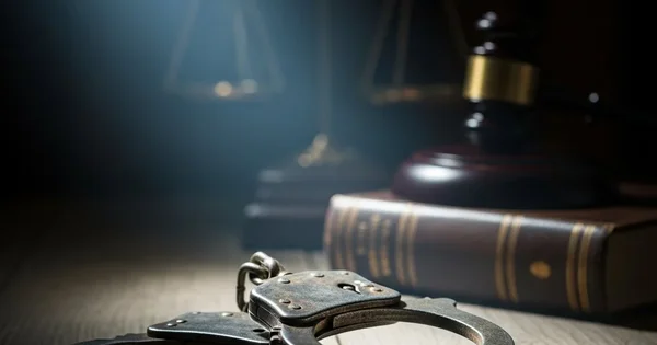 Handcuffs rest in front of a gavel and scales of justice.
