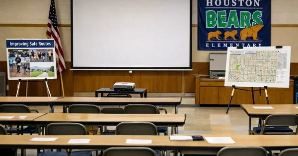A classroom is set up for a presentation on improving safe routes, with a map and school banner visible.