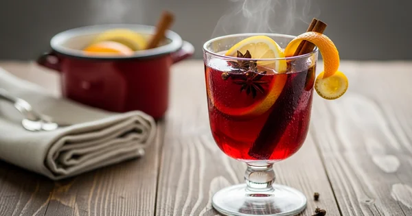 A glass of mulled wine garnished with orange and lemon sits on a wooden table.