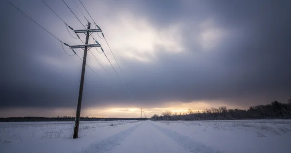 Power lines run alongside a rural road covered in deep snow following a winter storm.